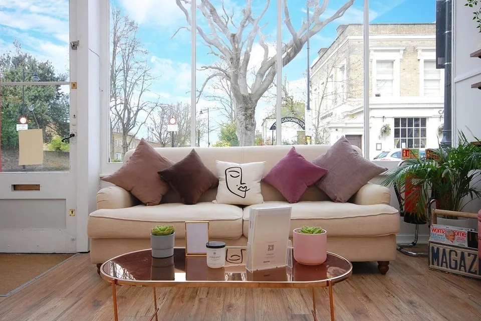 Canonbury Beauty waiting area with a sofa, cushions and large sash windows.